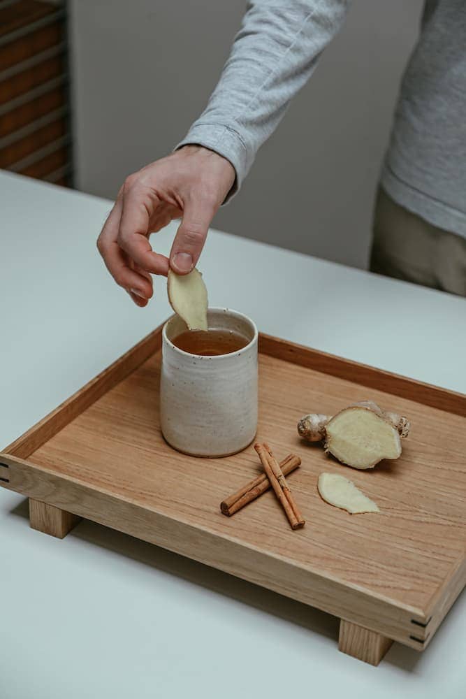 A cup of ginger tea with fresh ginger slices and a jar of honey on the side, used as natural remedies for sore throat relief.